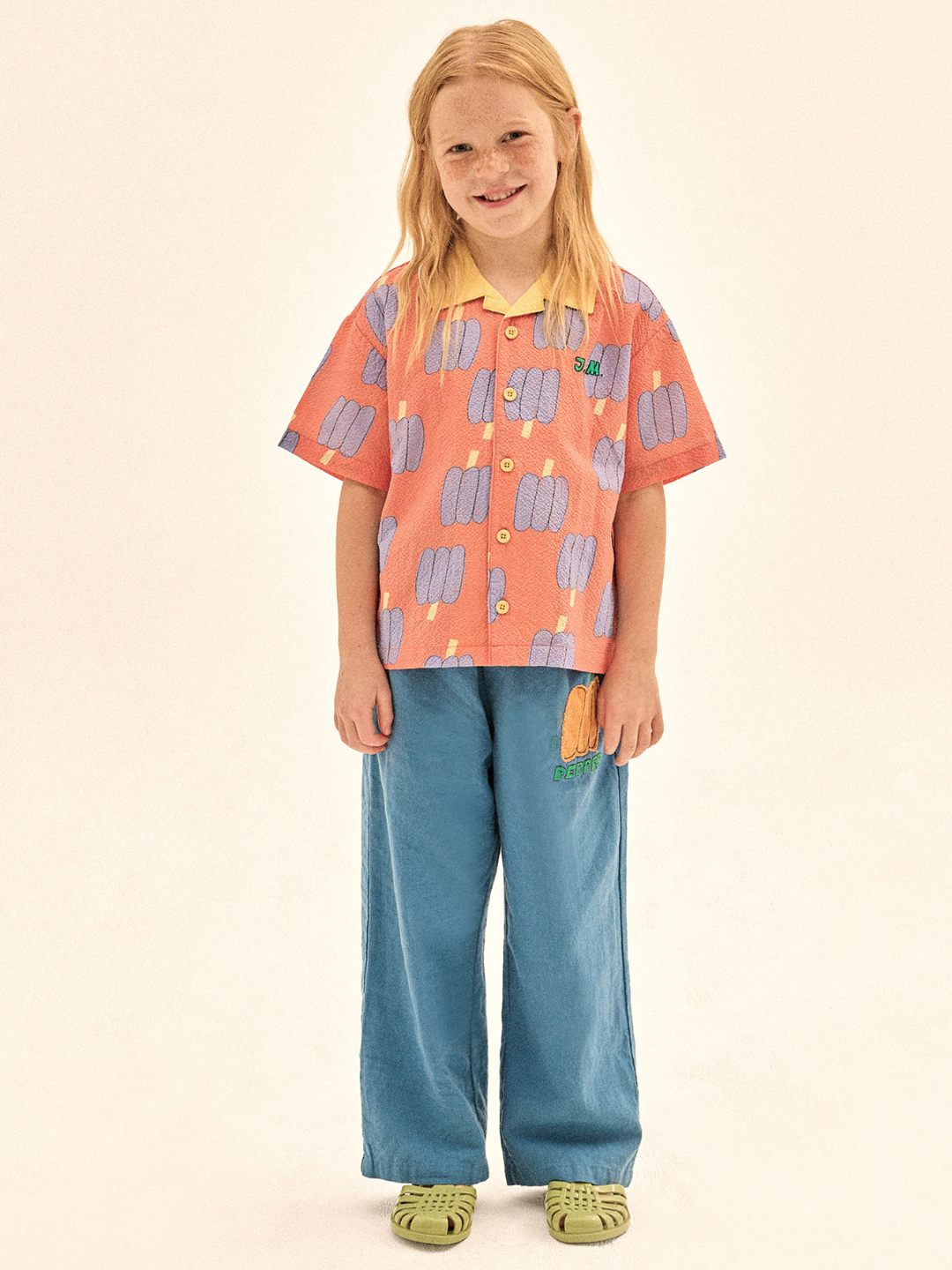 Child wearing a patterned shirt and blue pants on a beige background