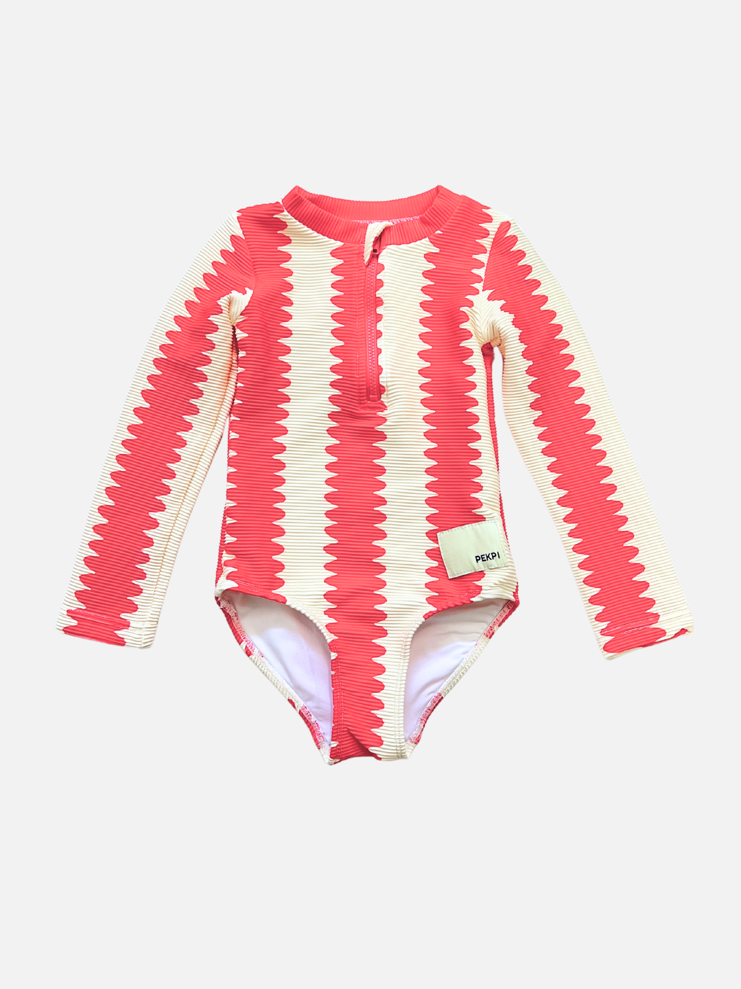 The FULL PIECE SWIMSUIT is a long-sleeve children’s swimsuit made from recycled material, with red and cream zigzag stripes, front button detail, and a waist tag.