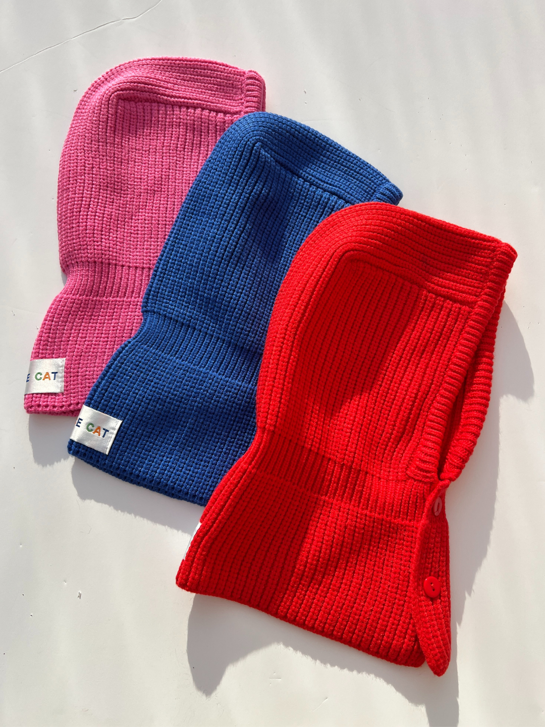 Red, Blue, and Raspberry balaclava laid flat on white background. 