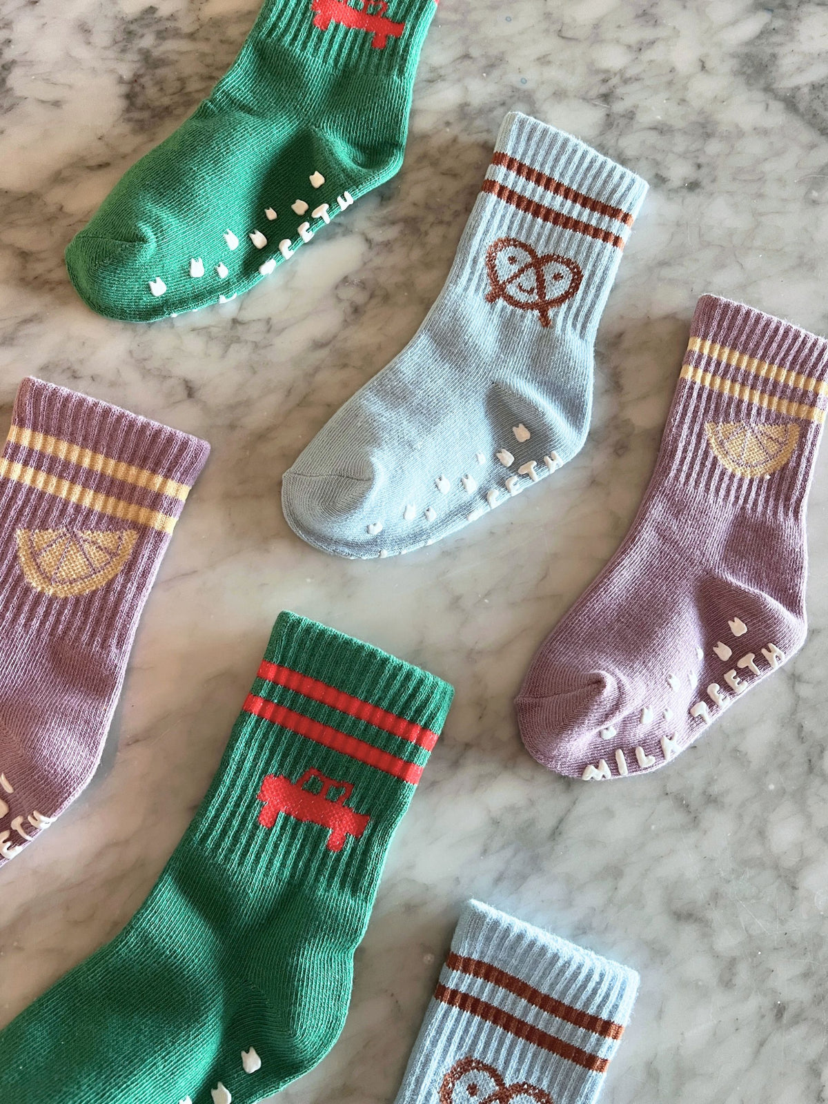 Five RIBBED GRIP SOCK crew socks with gripper soles, featuring patterns of a green car, a brown pretzel, and a yellow lemon wedge on green, blue, and purple fabric.