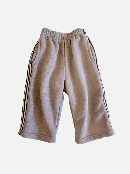 Image of The ALL DAY PANT features a relaxed fit with gray fabric, black side stripes, an elastic waistband, and two front pockets. Crafted from soft brushed cotton fleece on a plain white background.