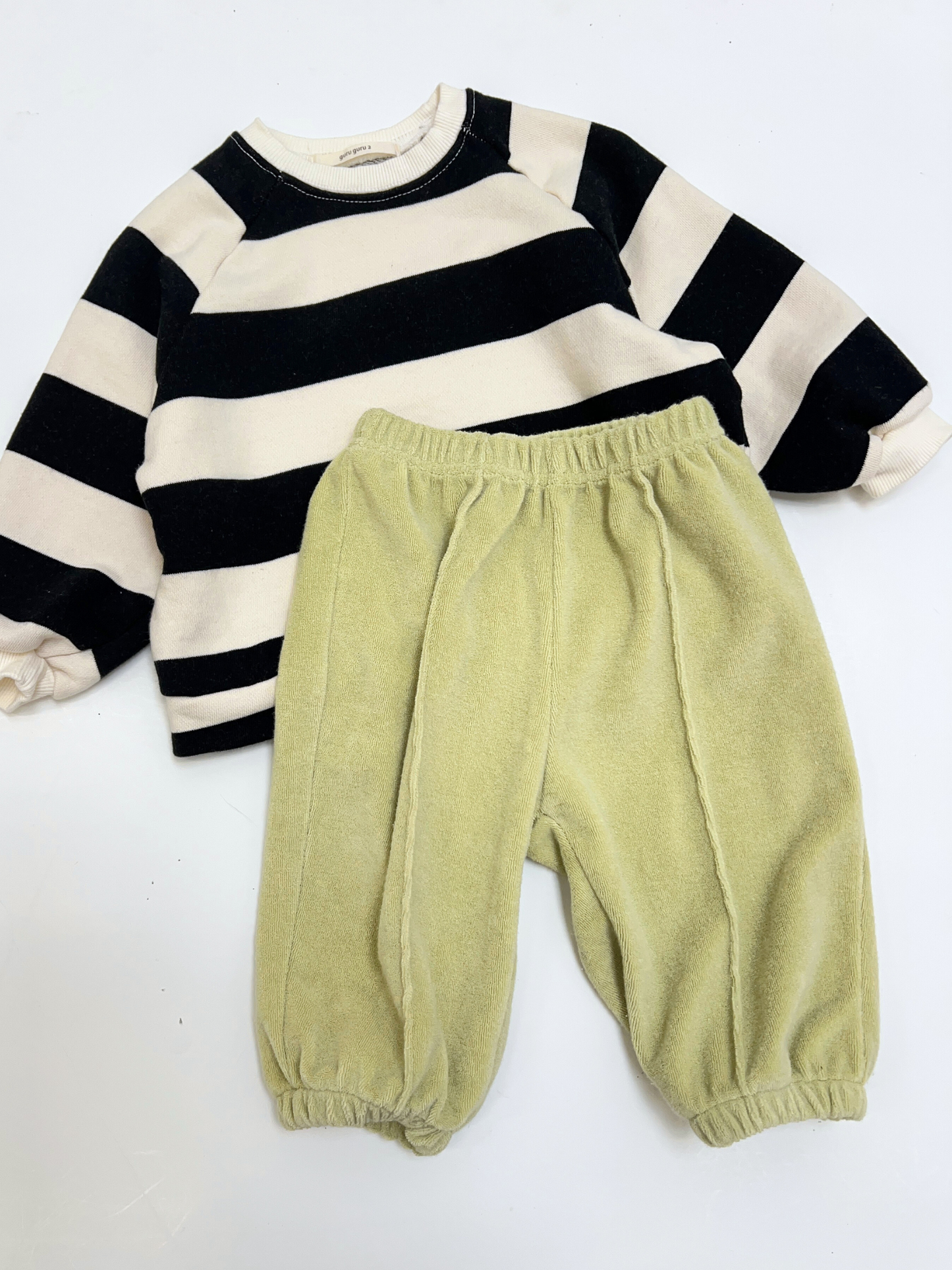 Black | The STRIPE BABY SWEATSHIRT in black and white stripes is paired with light green elastic-waist pants, both laid flat on a white background.