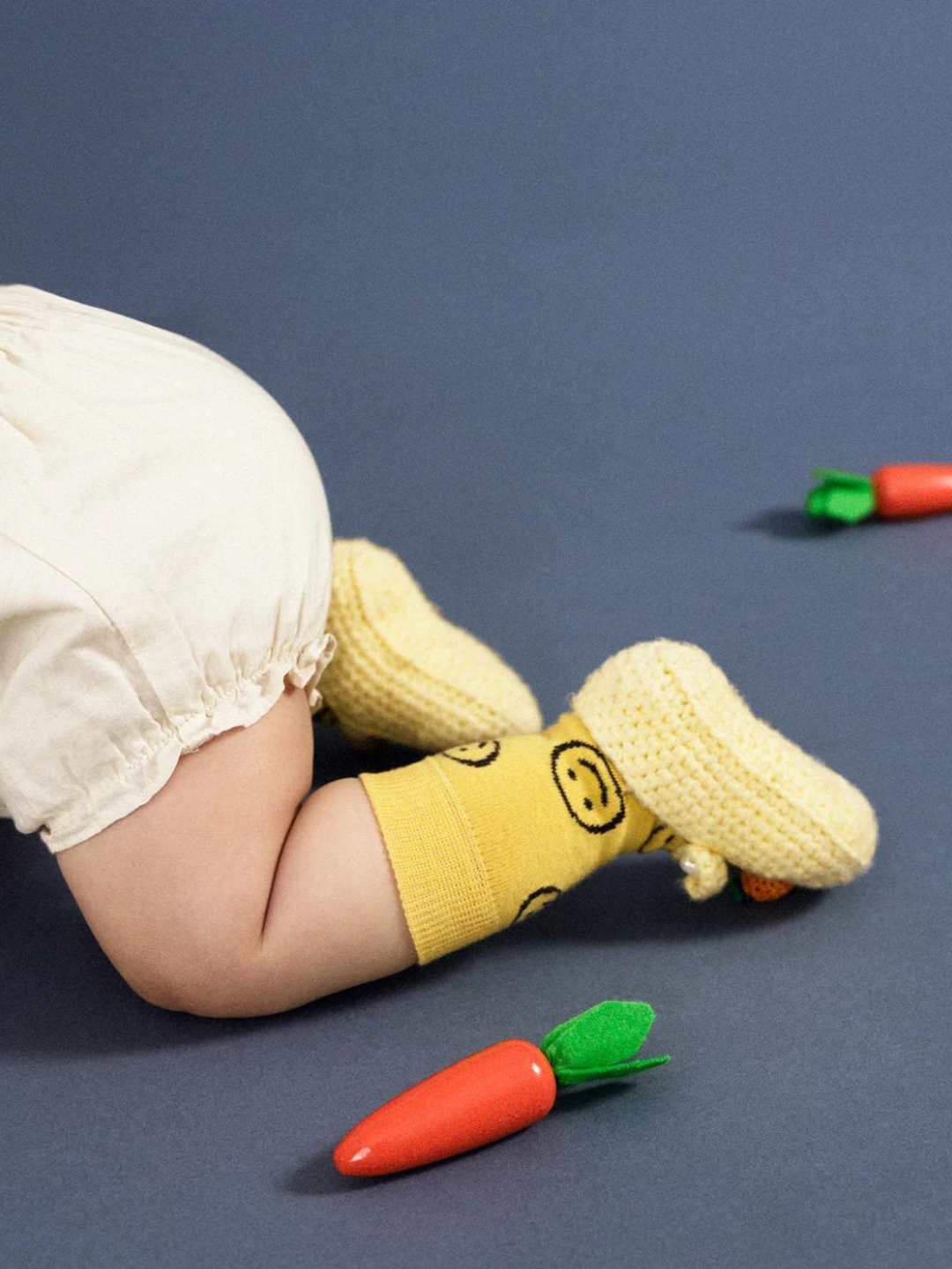A baby crawling in a pair of kids' ankle socks in yellow, printed with black smileys
