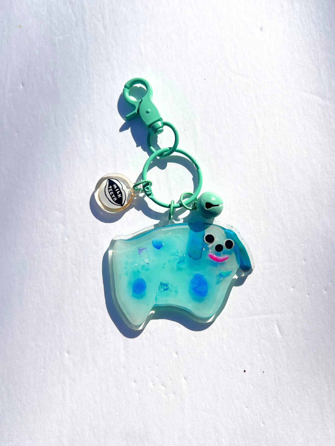The SOUVENIR KEYCHAIN is a blue, dog-shaped resin charm with spots, a smiley face, bell, and "Thank you" charm. Inspired by Katie Kimmel, all pieces hang from a pale green clasp keyring for cute bag accessories.