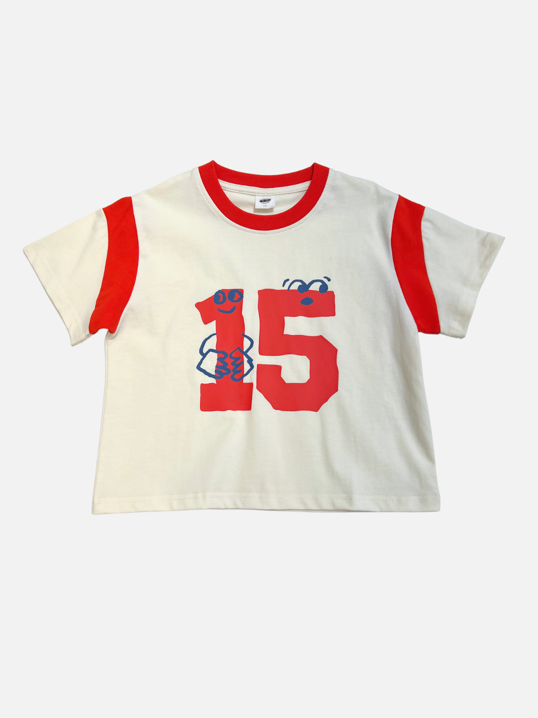 The VARSITY TEE is a white cotton t-shirt with red sleeve stripes and collar, a bold red number 15, and a small blue graphic on the front. It features an oversized boxy fit for a classic sports jersey look.