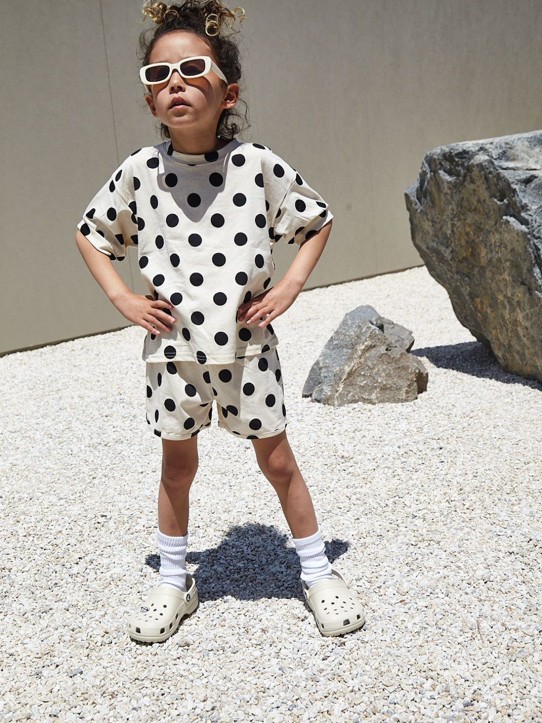  A child wearing a kids' tee shirt and shorts set in a pattern of black dots on an ecru background