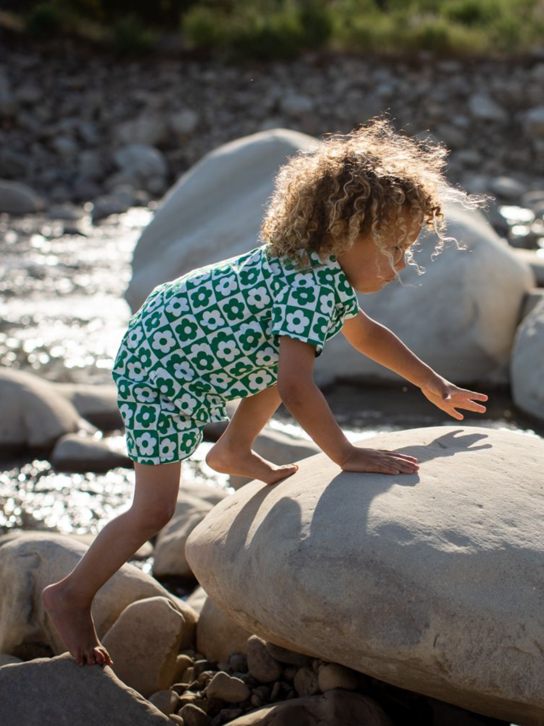 Child climbing over rocks wearing a kids' shirt and short set in a checkerboard pattern of green and white flowers