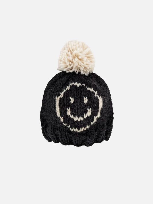 Image of Baby and kids beanie hat in chunky knit black yarn with an off-white smiley face on the front and an off-white pom-pom on top.