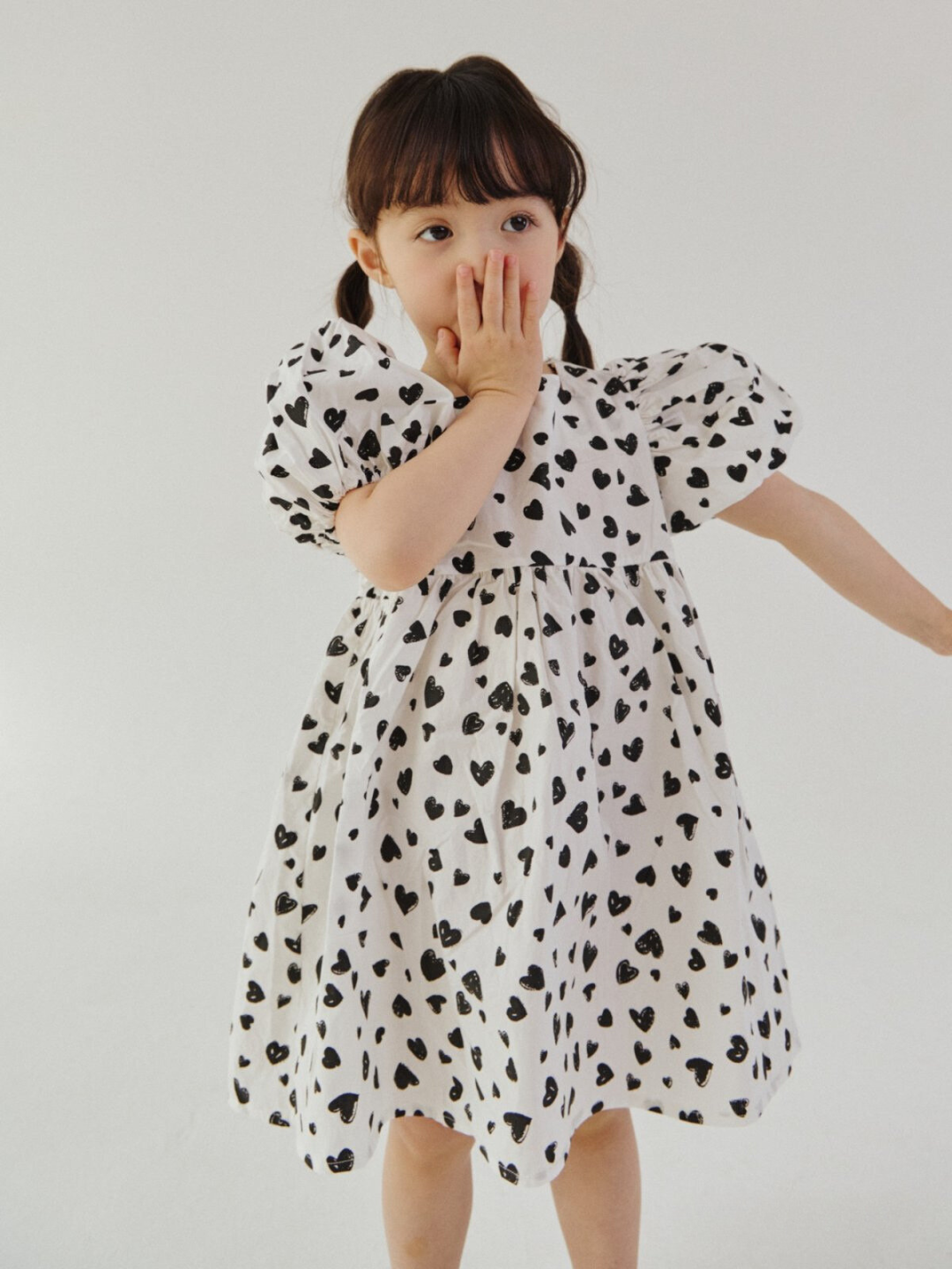 A child wearing a kids' puff-sleeved dress in a pattern of black hearts on a white background