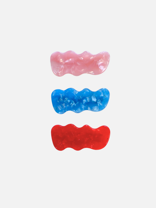 Image of The SQUIGGLE HAIRCLIP SET features three wavy rectangular plastic barrettes in pink, blue, and red, displayed vertically on a plain white background—stylish hair accessories for any look.