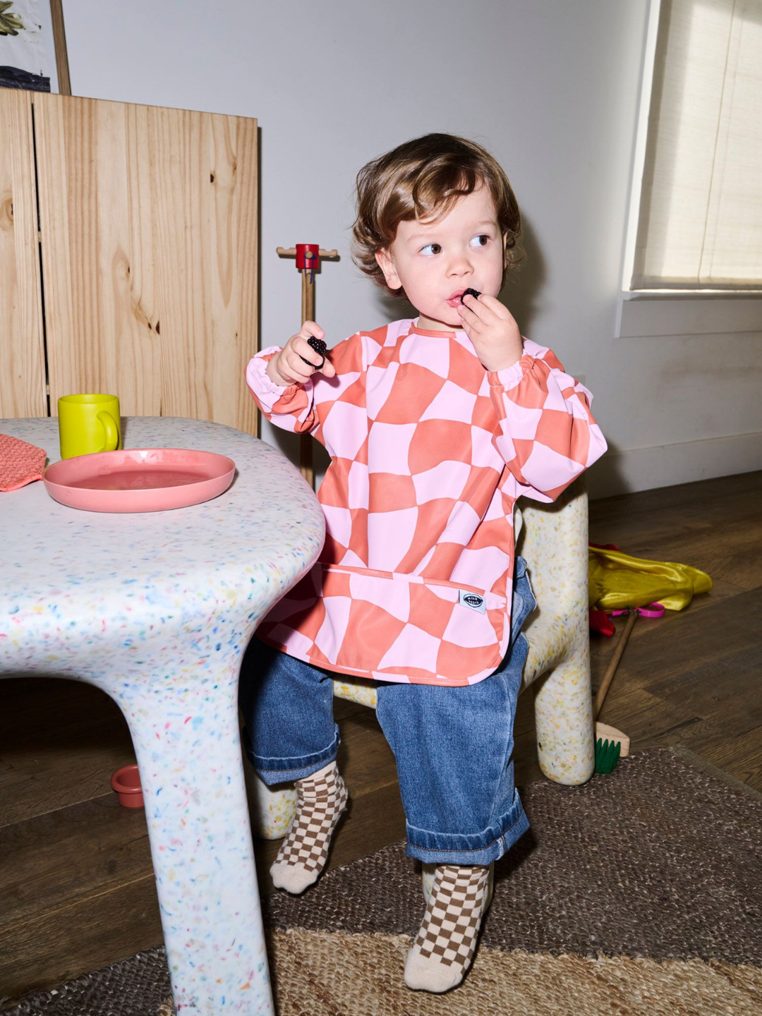 Pink Checkers | A child wearing the long sleeve light pink and rust wavy checked bib with a front pocket.