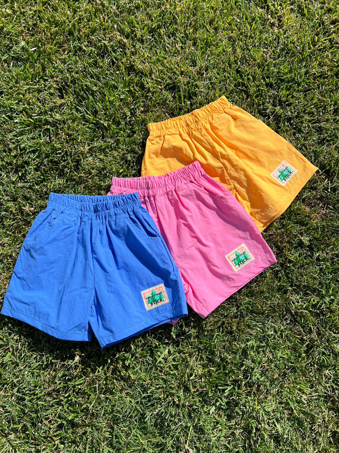 Mango | Blue Raspberry | Blue, pink and orange kids' shorts arranged on grass.