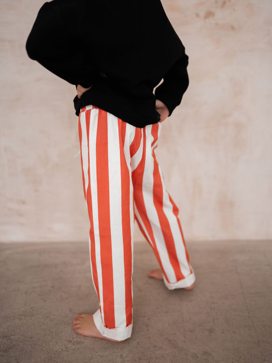 A person wearing the RED BLOCK STRIPE PANT along with a black hoodie, from our new arrivals collection, stands on a light-colored floor with hands on hips. The upper body is not visible.