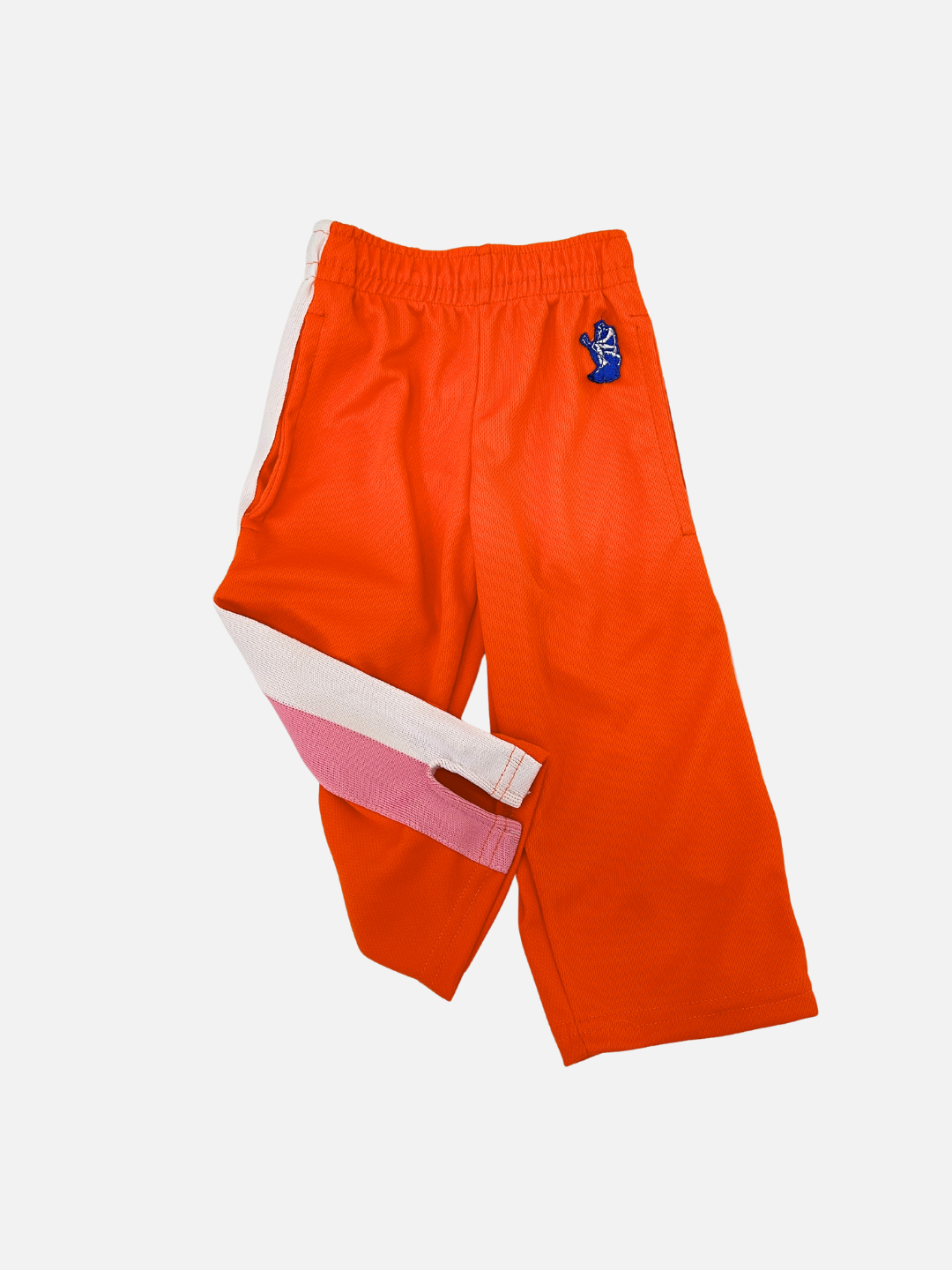 Orange | Discover the RELAX PANTS from Relax Lacrosse Brand, designed for kids in a bold orange hue. These pants are enhanced with a distinctive white and pink stripe along one leg and include an elastic waistband for a comfortable fit. Made from Miracle Mesh fabric to ensure maximum comfort, they are adorned with a small blue patch on the front. Ideal for active young explorers!