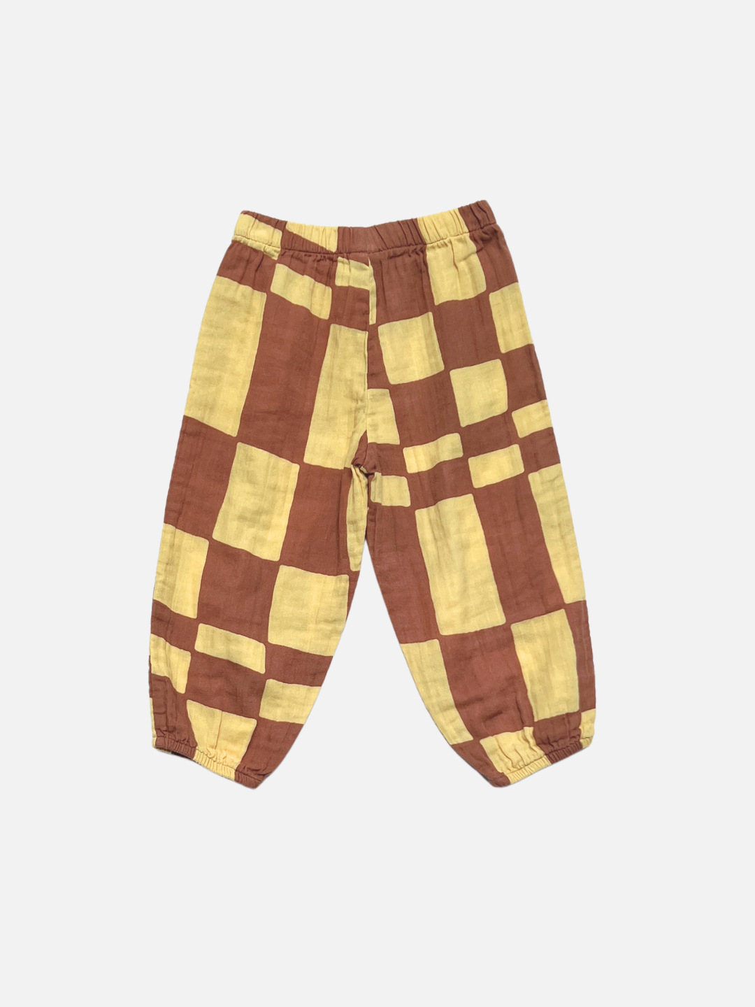 The MUSLIN PULL ON PANT features a loose fit, elastic waistband and cuffs, and a vibrant yellow and brown checkerboard print. Crafted from soft organic cotton muslin, these toddler joggers are shown laid flat on a white background.