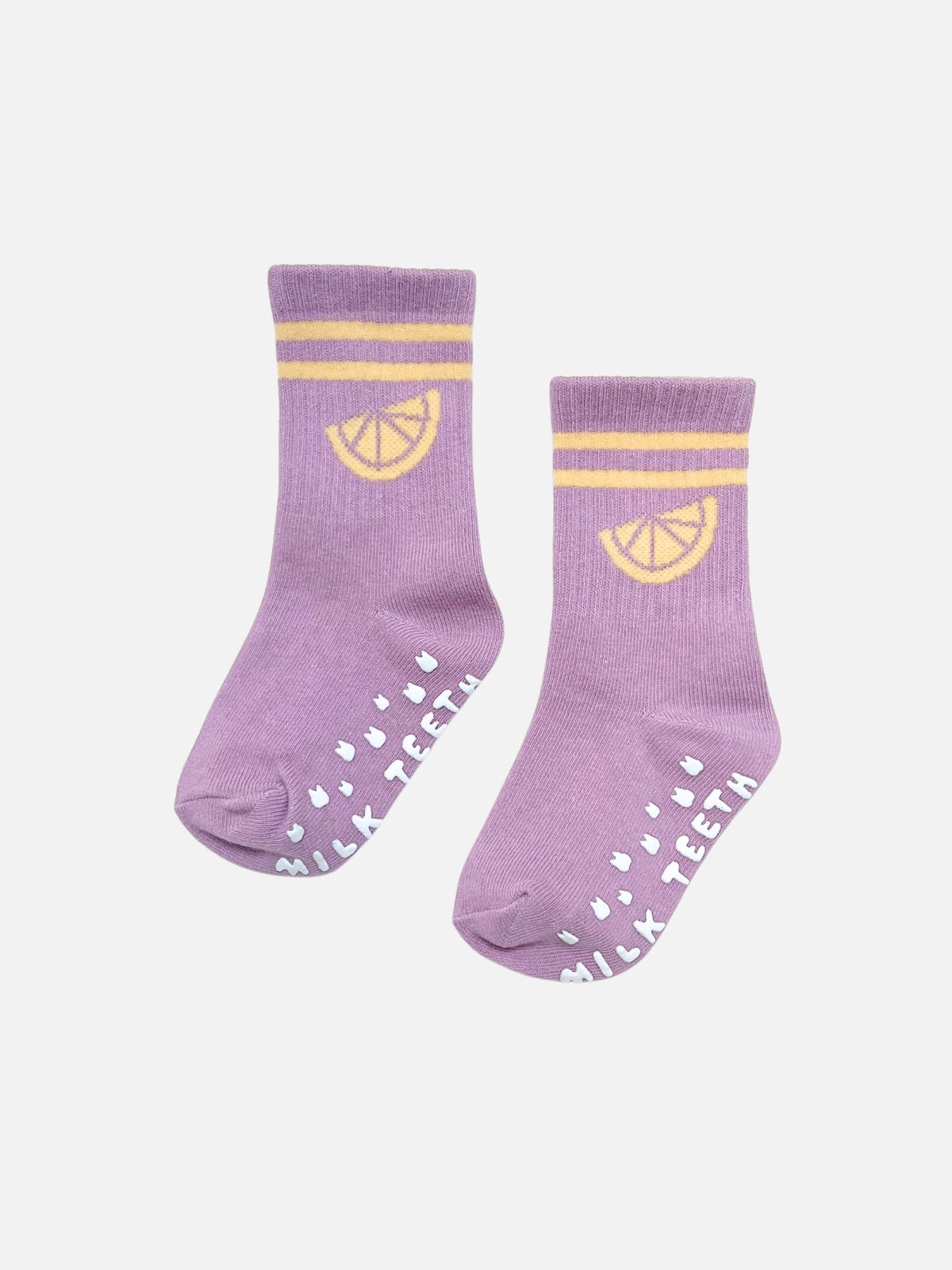 Pair of lavender RIBBED GRIP SOCK cotton socks with yellow stripes, a lemon slice graphic, and white text on the soles reading “MILK TEETH.”