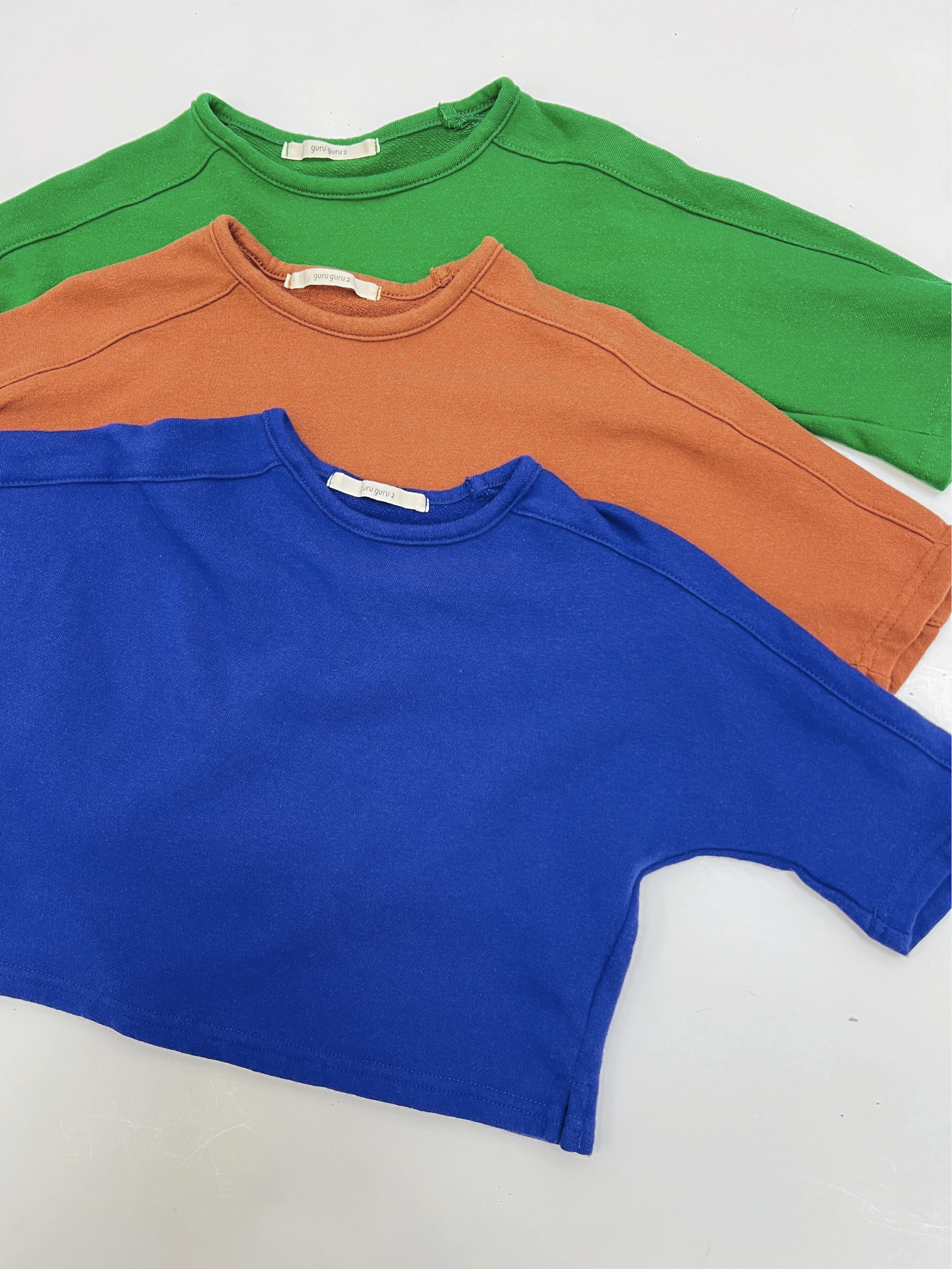 Three BABY BOATNECK LONGSLEEVE shirts in green, orange, and blue—crafted from soft terry cotton by a popular Korean baby brand—are displayed overlapping on a white surface.