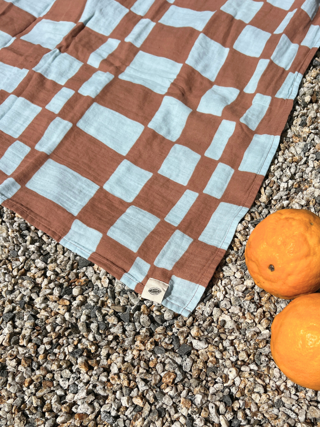 Checkered fabric with brown and light blue pattern on a gravel surface with oranges.