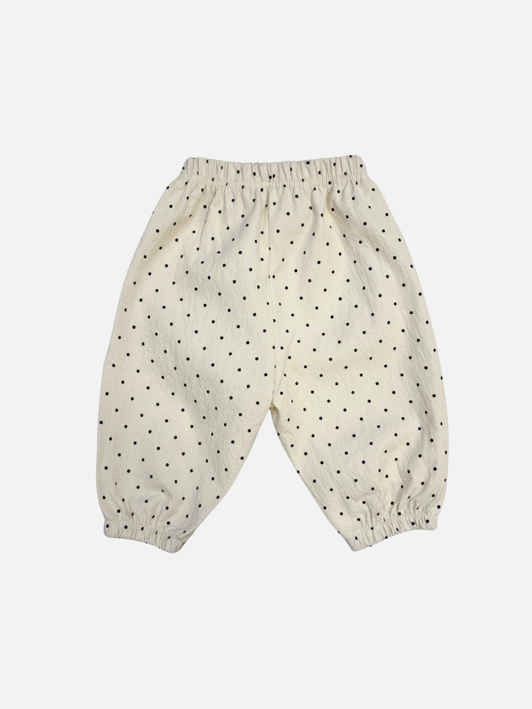The BABY PULL-ON PANT features white woven cotton with black polka dots, an elastic waistband, and cuffs for comfort. These baby pants are shown on a plain white background.