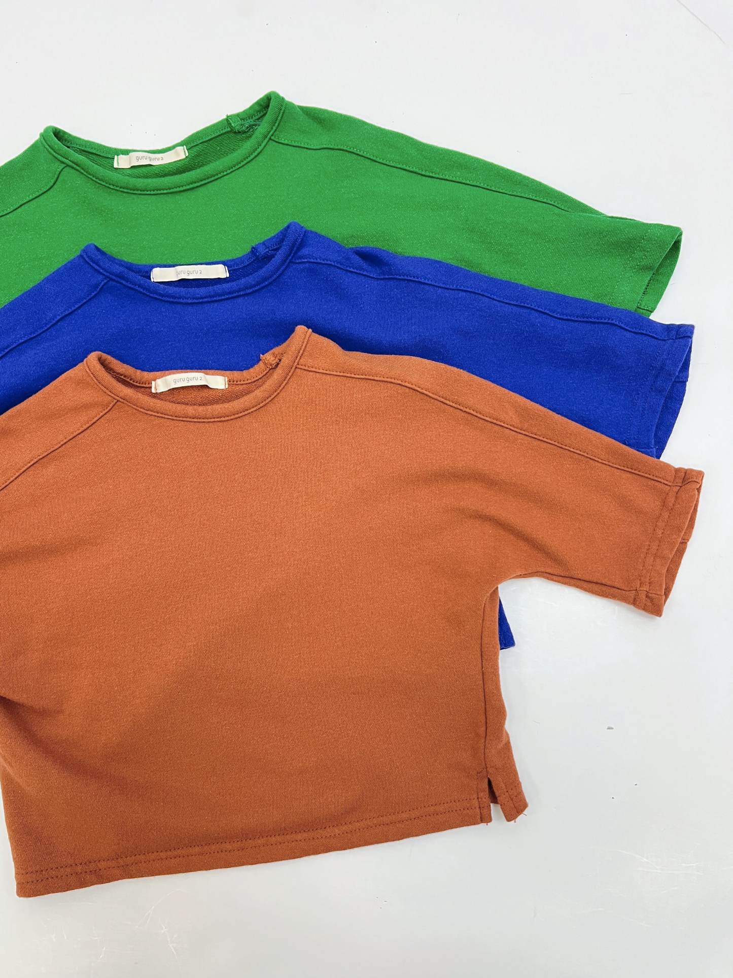 Brown | Three BABY BOATNECK LONGSLEEVE shirts in green, blue, and rust orange—crafted from soft terry cotton and inspired by a leading Korean baby brand—are laid flat on a white surface, slightly overlapping.