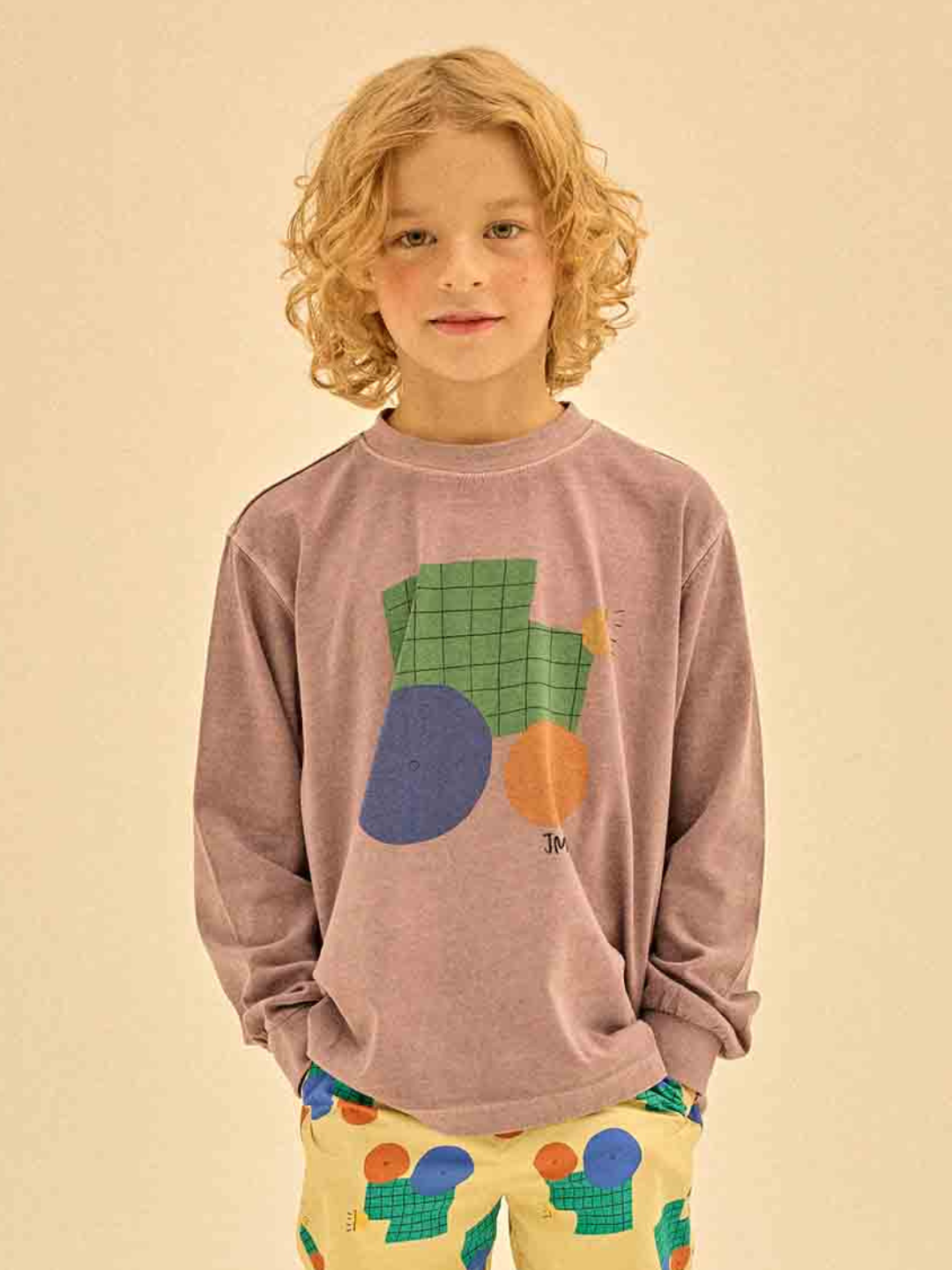 Child with curly hair wearing a TRACTOR PIGMENT LONGSLEEVE T-SHIRT, featuring abstract shapes in a soft pink hue, and matching patterned pants, standing against a neutral background.