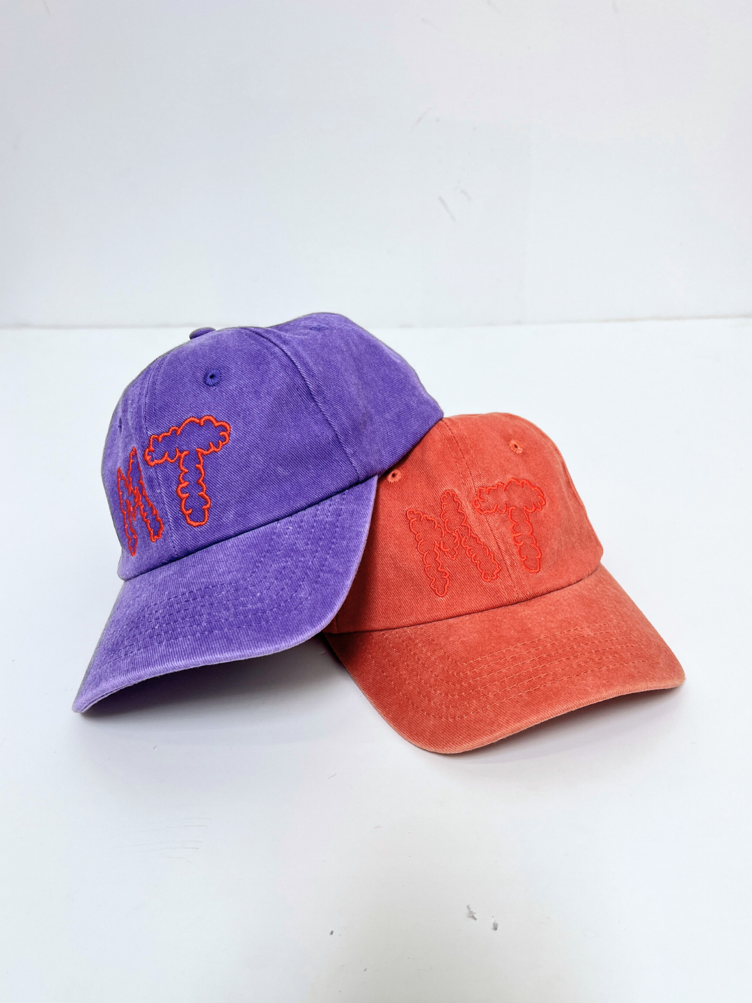 The MT DAD CAP, shown in purple and orange cotton canvas with "MT" for Milk Teeth embroidered on the front, is displayed against a plain white background.