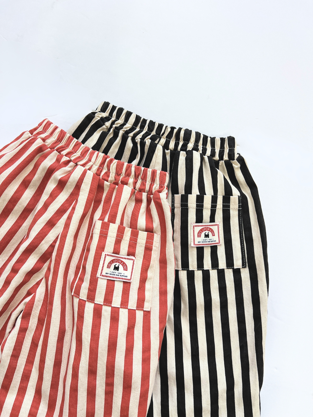 The LICORICE STRIPE PANT comes in two pairs: one red and white, one black and white. These cropped, barrel-leg pants feature elastic waists, front pockets, and a small rainbow patch for playful style and comfort.