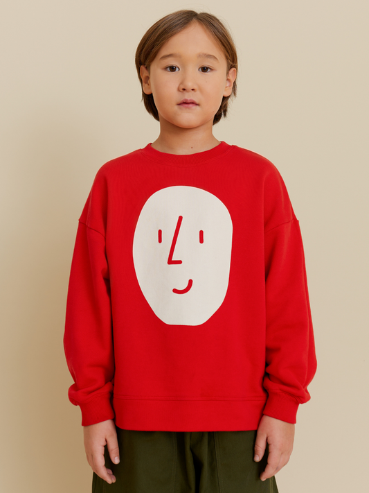 Second image of Red | The POTATO SWEATSHIRT in red is an oversized OXOX CLUB piece made from organic cotton, featuring a minimalist white smiling face graphic on the front.