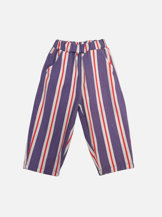 Image of The STRIPE TWILL PANT is a pair of children's cotton twill pull-on pants with vertical purple, white, and red stripes, an elastic waistband, baggy fit, and side pockets, shown on a plain white background.