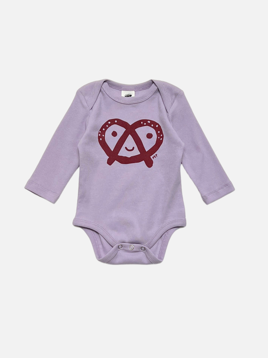 Image of Lavender PRETZEL LONG SLEEVE ONESIE featuring a red smiley pretzel graphic on the front, displayed against a plain white background.