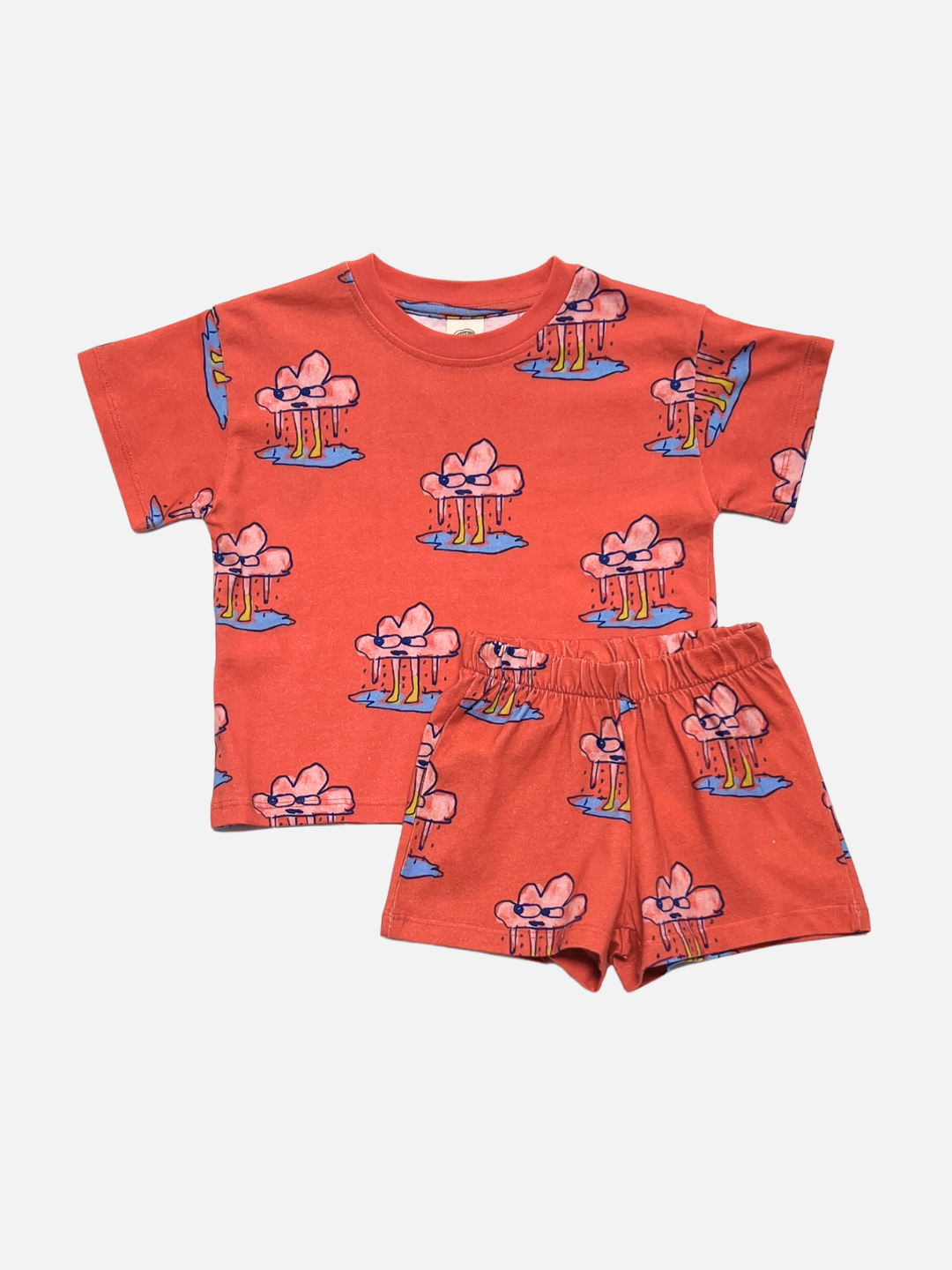The RAINY DAY SHORT SET is a children’s unisex matching t-shirt and shorts set in red, crafted from soft organic cotton. It features a playful, repeating rain cloud character—ideal for fun summer play.