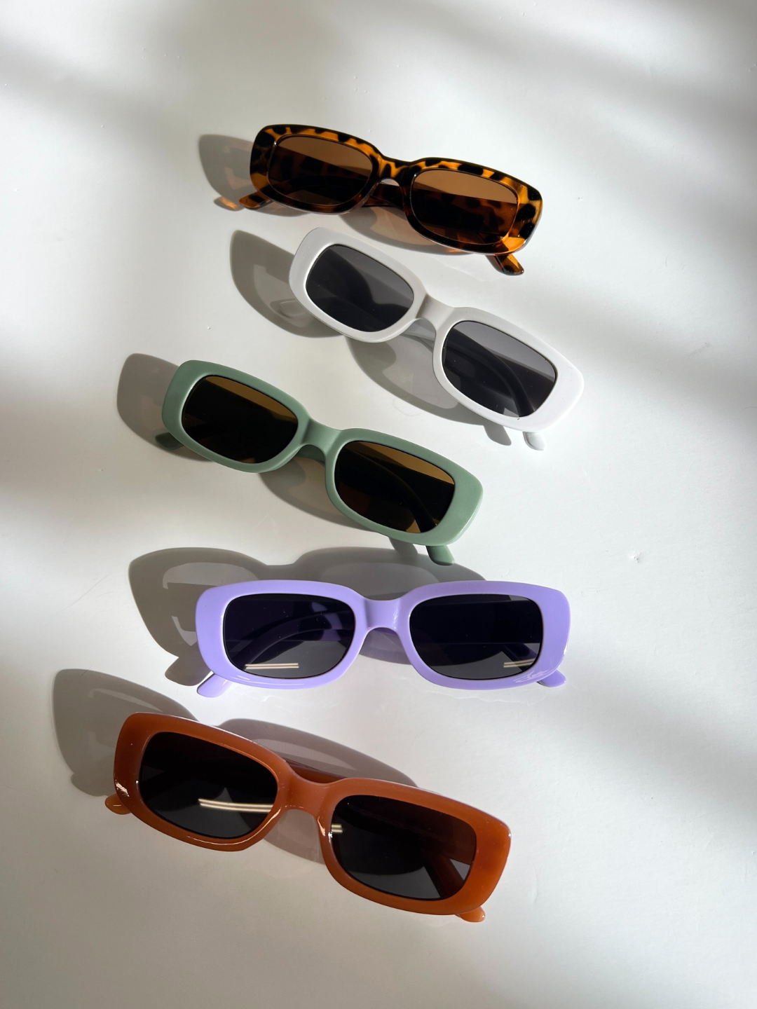 Terracotta | Five pairs of SANTA CRUZ SUNGLASSES, suitable for ages 2-6, are displayed vertically on a white surface. These stylish shades come in tortoiseshell, white, green, purple, and brown frames and feature UV400 lenses.