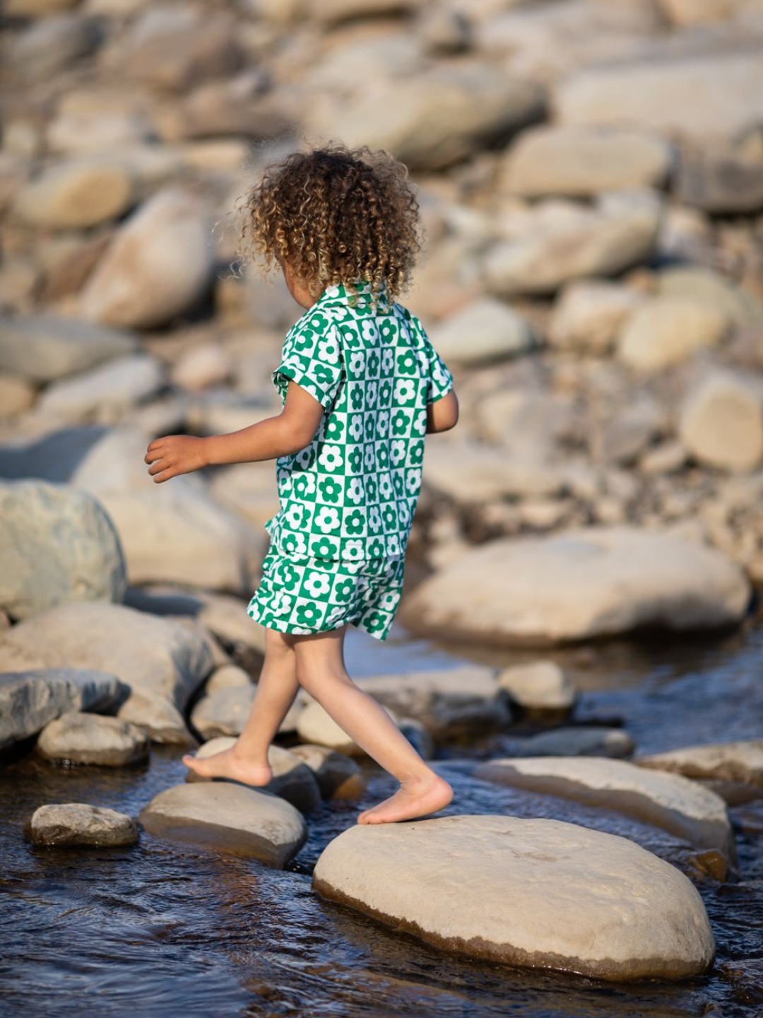 Child walking over stepping stones wearing a kids' short set printed in a checkerboard of green and white flowers