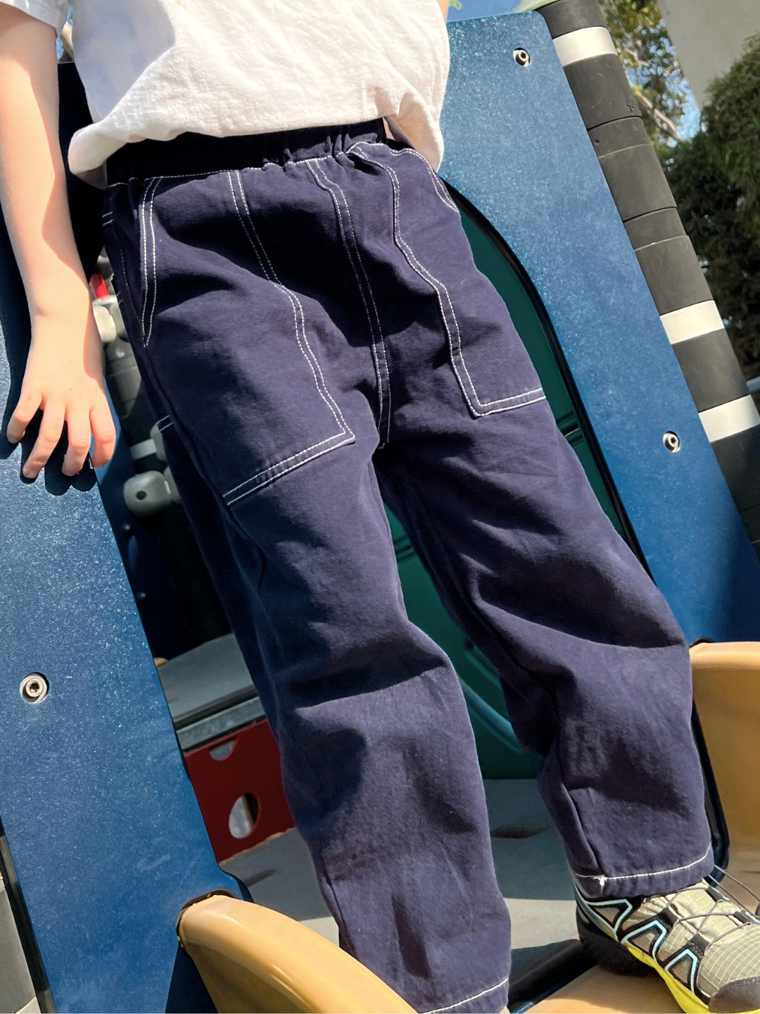 Navy | A child in TOPSTITCH TWILL PANTS with an elasticated waist and sneakers stands on a playground slide.