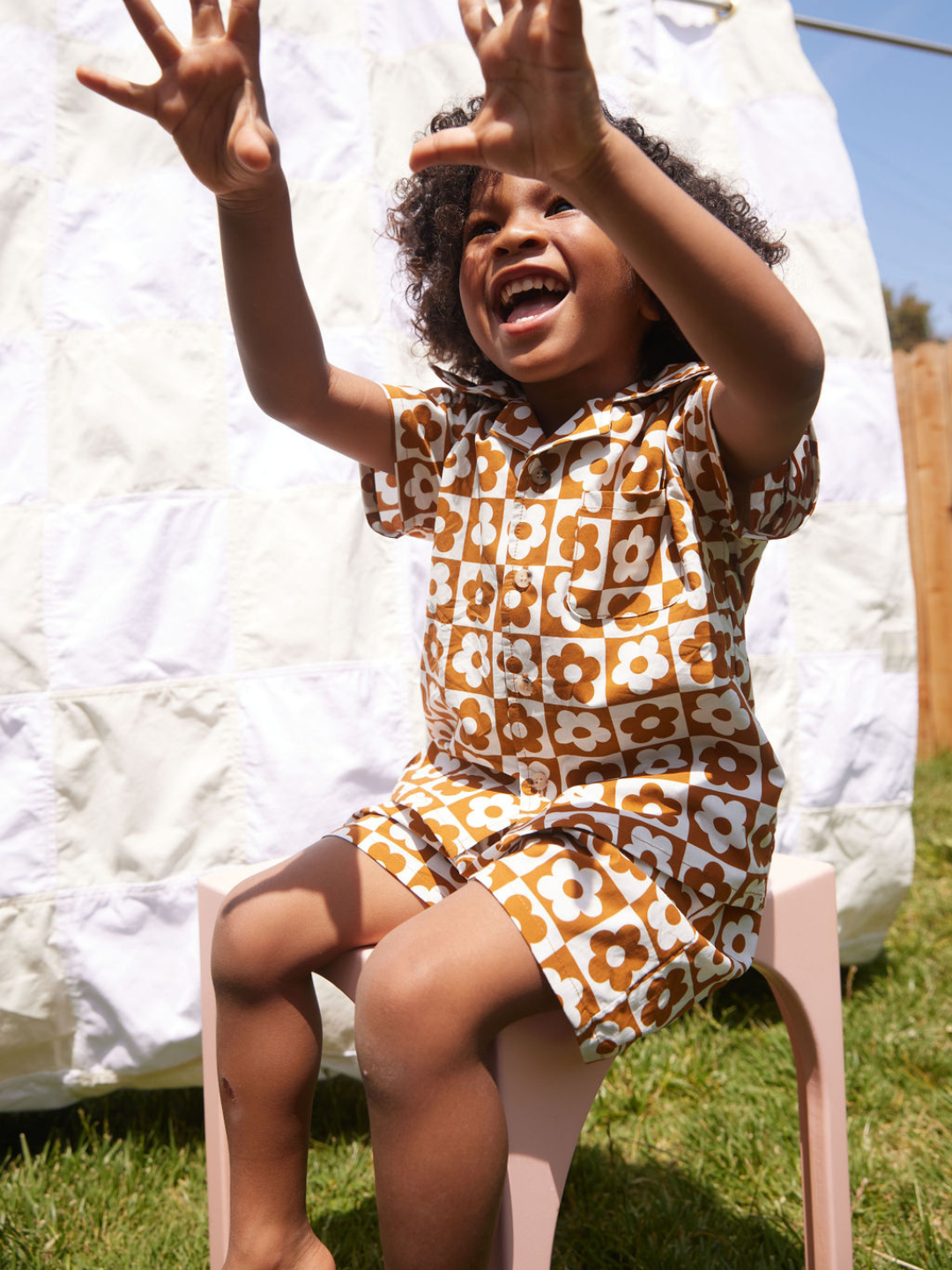 Seated child wearing a kids' shirt and shorts set in a checkerboard pattern of terracotta brown and white flowers