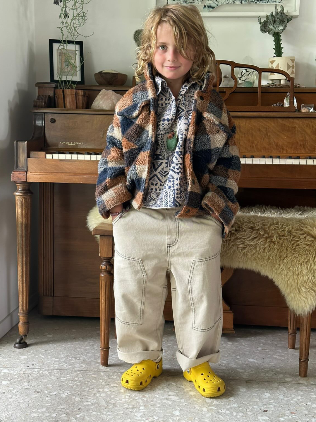 A Child is wearing Stone Stitch Jean with fuzzy checkered jacket, printed shirt, and yellow crocs. 