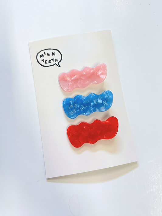 Second image of The SQUIGGLE HAIRCLIP SET features three wavy rectangular plastic barrettes in pink, blue, and red, displayed vertically on a plain white background—stylish hair accessories for any look.