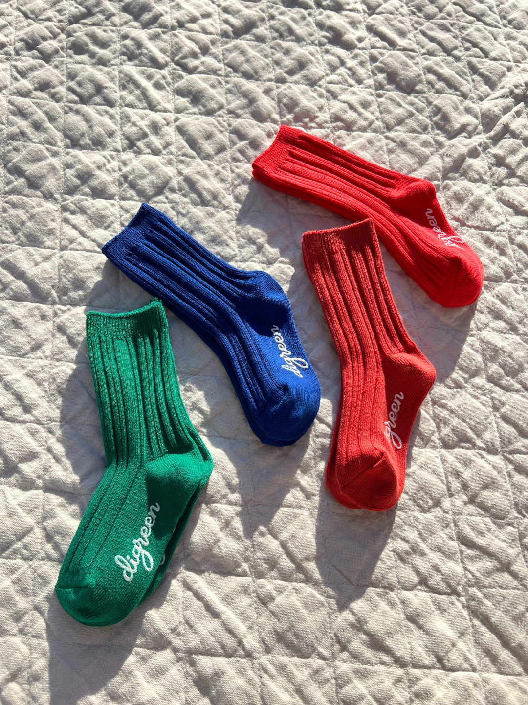 Four socks of each color of the kids' Pigment socks set laid in the sun on a quilt.