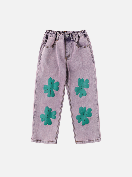 Image of The LUCKY CLOVER DENIM PANTS are light purple jeans with an elastic waistband and four large green clover appliqués on the front, shown on a plain white background.