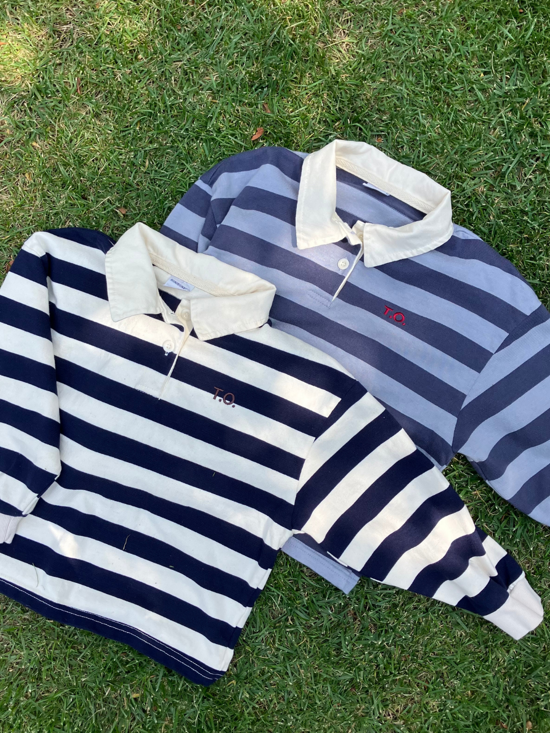 Cream | Two RUGBY LONGSLEEVE shirts with white collars are laid on grass. One shirt is navy blue and white, while the other is light blue and white. Both cotton jersey shirts from an acclaimed Korean kids brand feature a small "TO" logo on the chest.