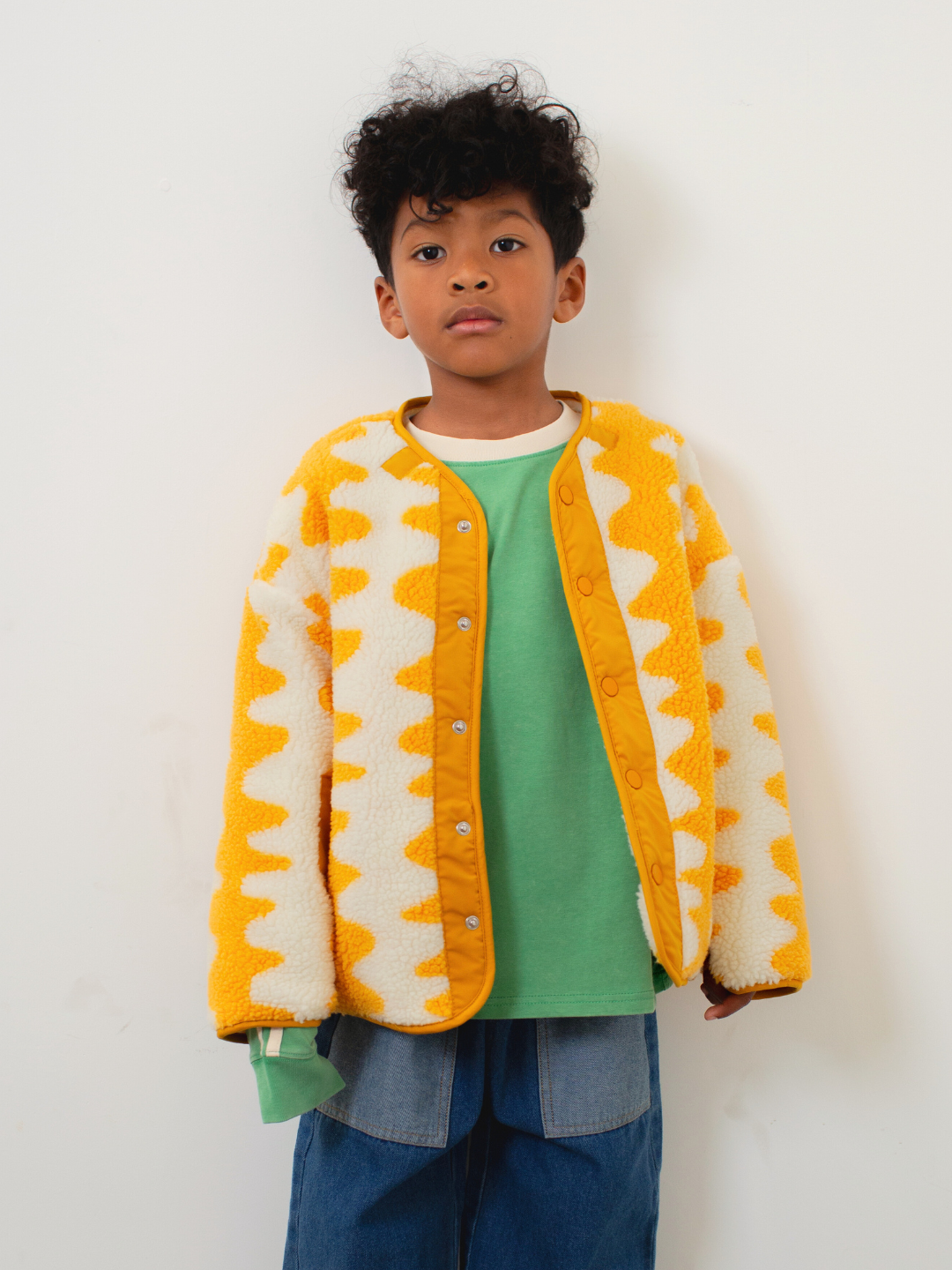 Child wearing a yellow and white patterned jacket on a white background