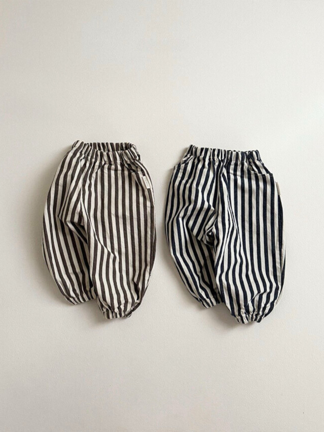 Charcoal Stripe | Two pairs of PIRATE PANTS are displayed against a white background. The pants on the left are gray and the ones on the right are black. Both feature elastic waistbands and cuffs, showcasing a trendy balloon leg design. A Minirobe exclusive for versatile, stylish comfort.