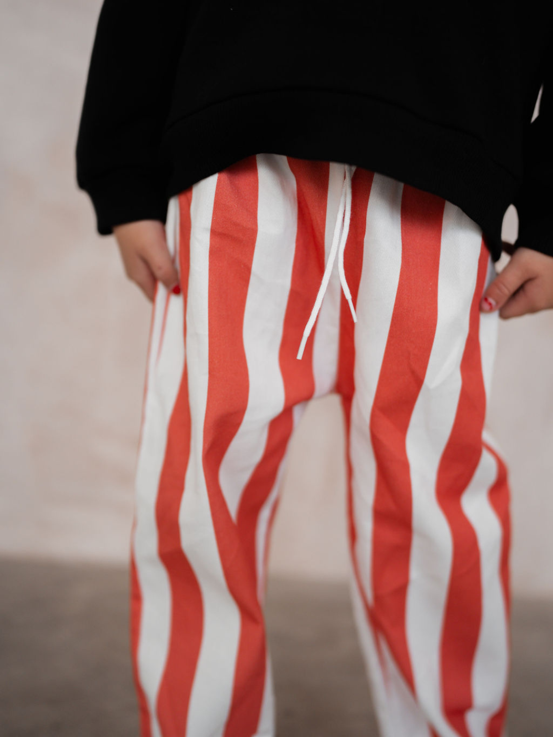 A person wearing the RED BLOCK STRIPE PANT from our new arrivals collection, paired with a black top. The image is cropped to show only the lower torso and legs.