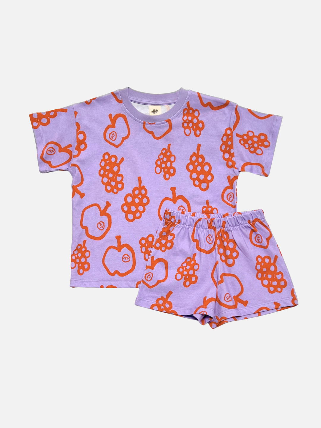 The FRUIT STAND SHORT SET is a kids' matching outfit with a short-sleeve shirt and shorts, showcasing colorful apple and grape prints on a purple background, displayed on a plain white surface.