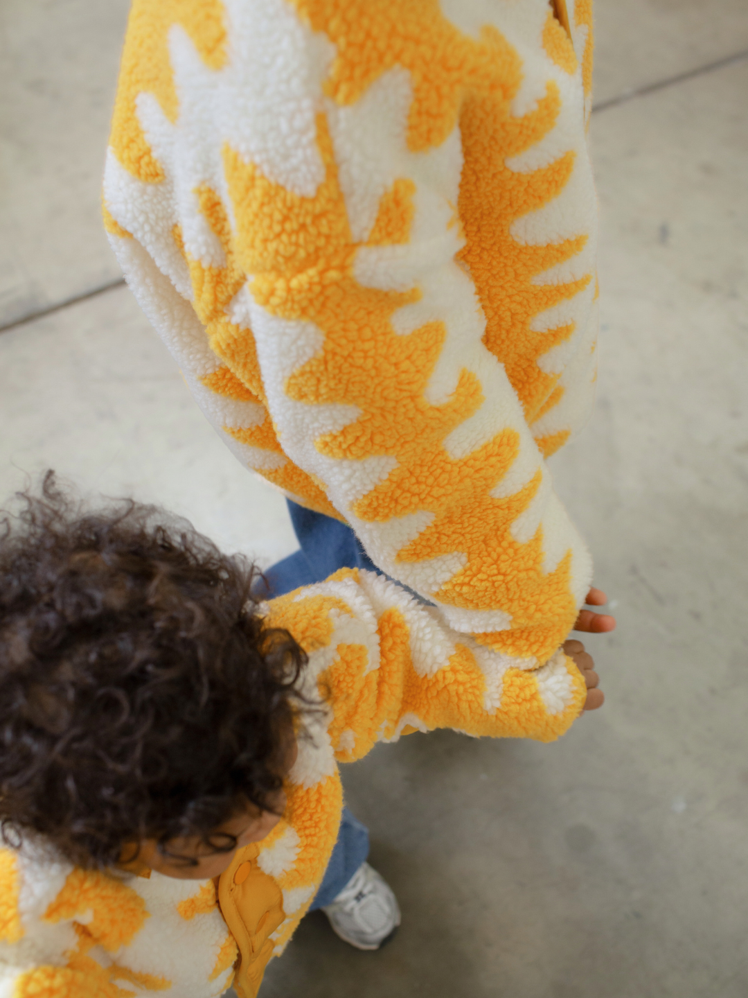 Child wearing a yellow and white patterned onesie on a concrete floor.