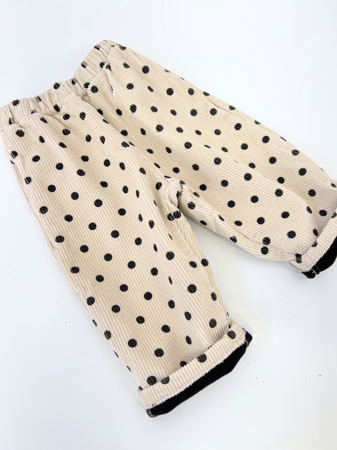 Ecru | The FLEECE-LINED DOT CORDS, designed by a popular Korean kids brand, are a pair of beige corduroy pants adorned with black polka dots. They feature an elastic waistband and folded cuffs and are stylishly presented on a white background.