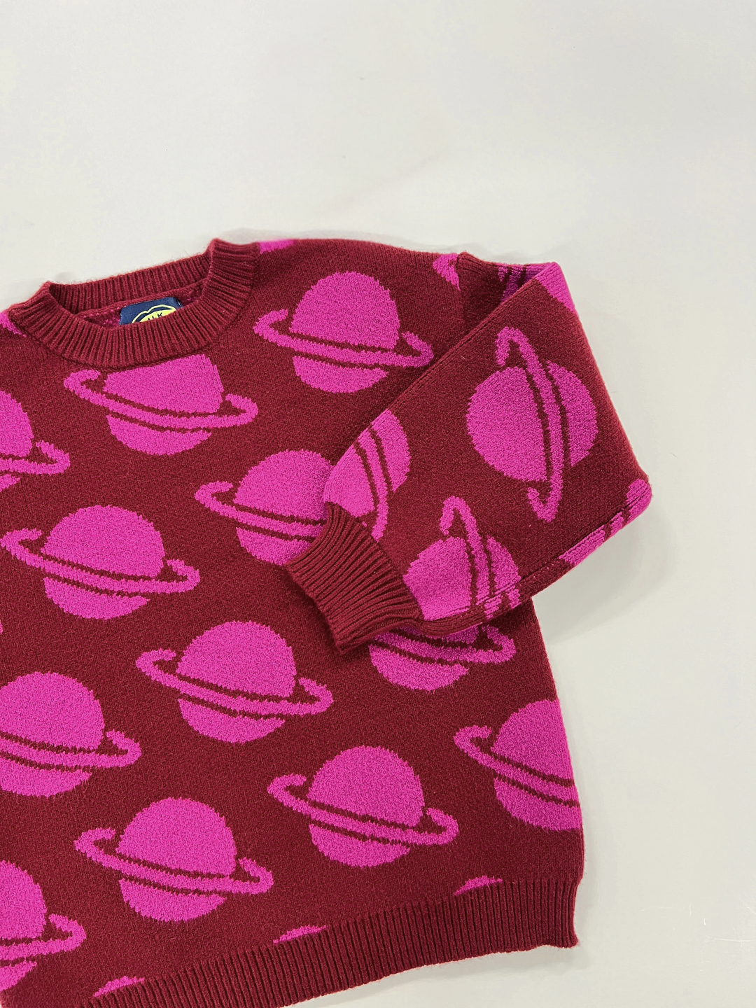 Maroon | The SPACE CAMP SWEATER, featuring a maroon hue adorned with a pink ringed-planet pattern, is elegantly displayed on a light surface. For detailed measurements and closer looks, please refer to the additional photos provided.