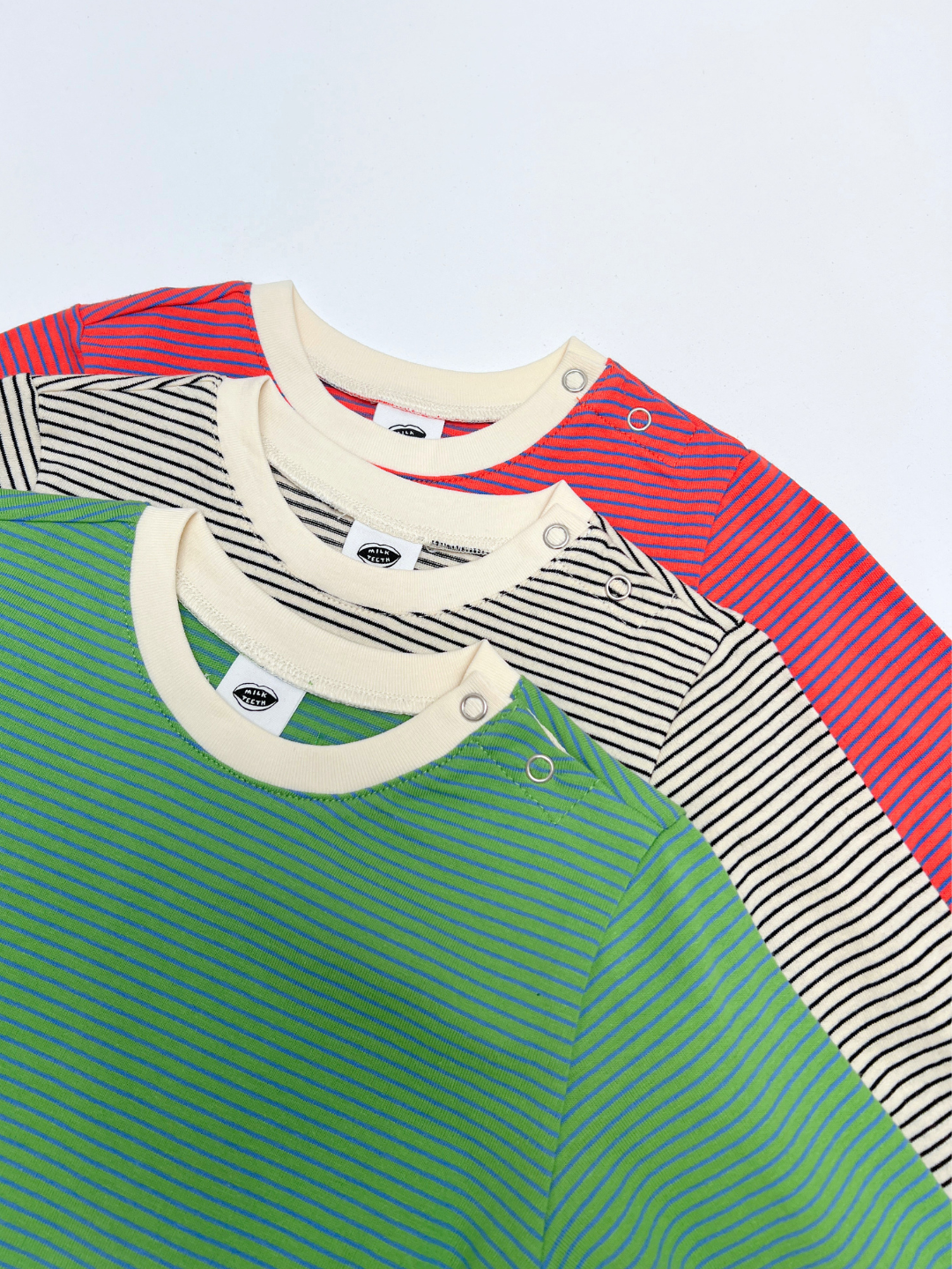 Three BABY STRIPE LONGSLEEVE shirts—green, beige, and red—are stacked diagonally, each featuring thin horizontal stripes and two metal snap buttons on the left shoulder for easy dressing. Crafted from soft cotton jersey, these baby and toddler essentials are both comfortable and practical.