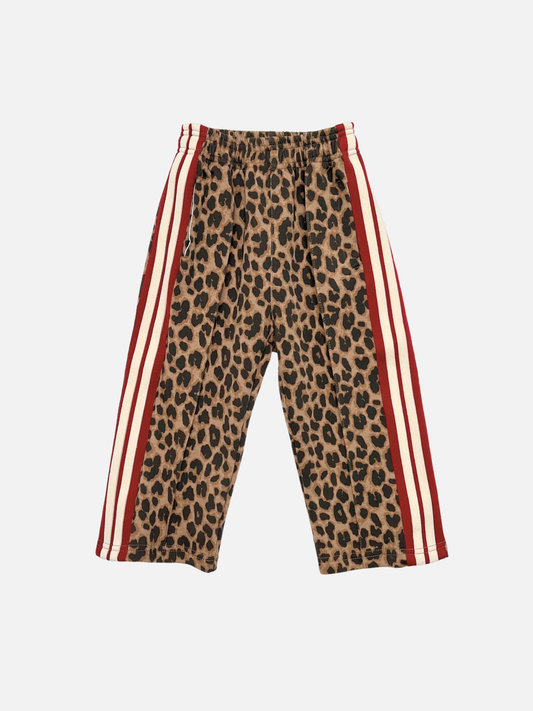 Image of A pair of kids track pants featuring a brown and black leopard print pattern, with red and cream vertical stripes running down the sides, shown against a light gray background.