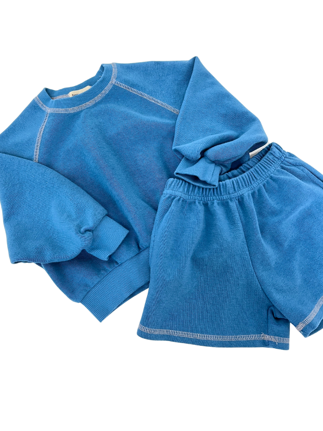 Blue | Cantucci Studios introduces the VARSITY SWEATSHIRT set, featuring a retro-style blue sweatshirt and matching shorts made from soft brushed cotton with white stitching, displayed on a white background.